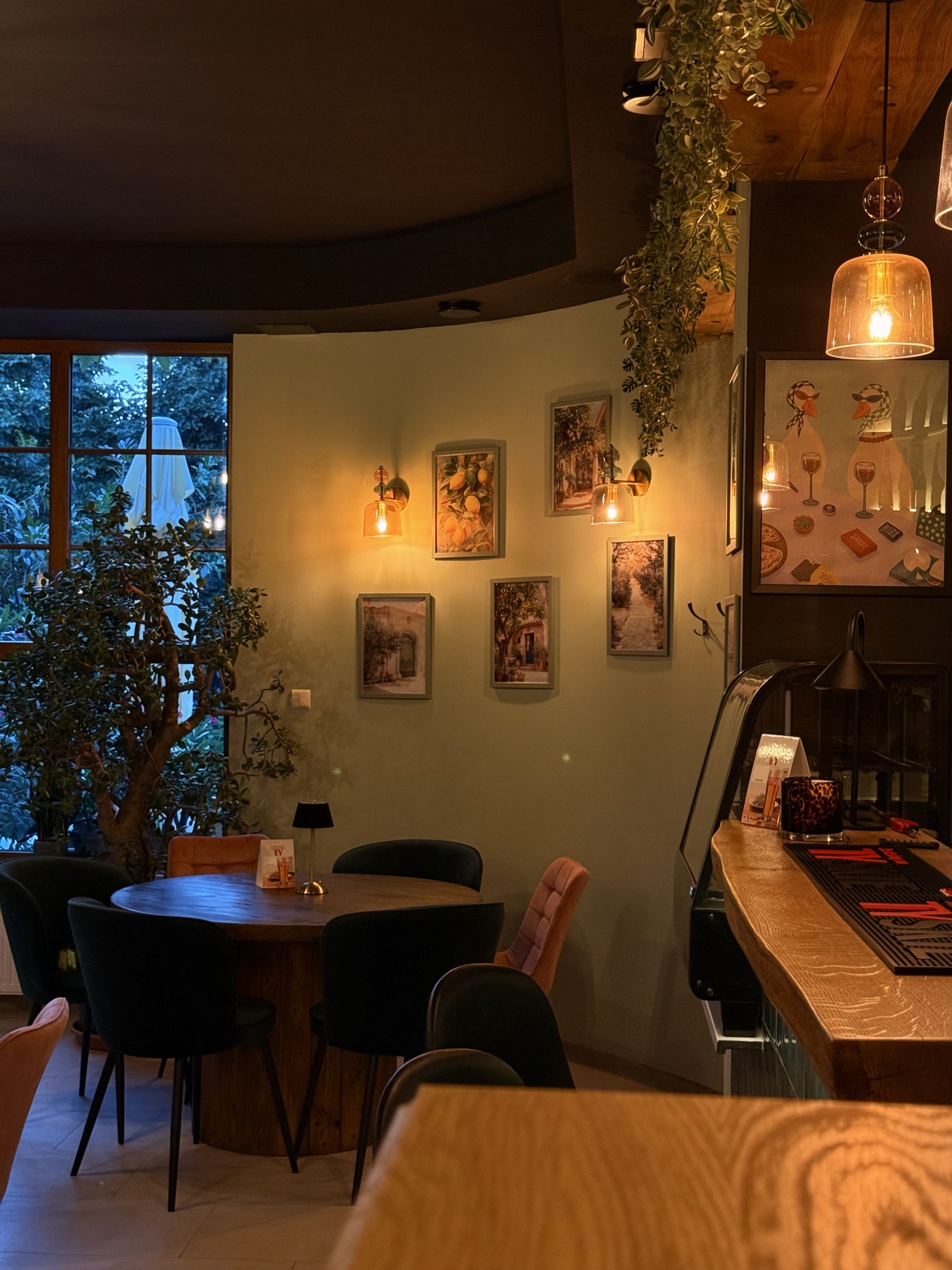 Narożnik sali Pizzerii Ogrodowej w Wieluniu — okrągły stół, obrazy i zieleń